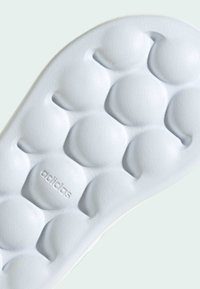 Biela gumená podrážka tenisky s okrúhlymi textúrovanými výčnelkami, jemným brandingom a hladkými kontúrami pre pohodlie a priľnavosť.