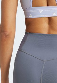 Sivé legíny s vysokým pásom a kontrastnými švami, vybavené pásom s logom na vrchu a hladkou elastickou textúrou.