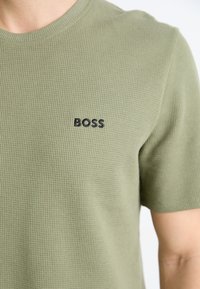 Maslinasto zeleni T-shirt kratkih rukava od teksturirane, rebraste tkanine sa malim crnim logotipom "BOSS" na prsima. Ležeran dizajn.