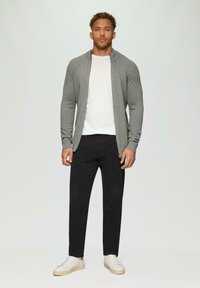 Grauer Reißverschlusscardigan über einem weißen T-Shirt, kombiniert mit schwarzen Hosen und weißen Sneakers. Einfaches Design und weiche Textur.