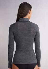 Langsleeve geribbelde coltrui van donkergrijze stof. Heeft een aansluitend ontwerp met een hoge kraag en een soepele textuur.