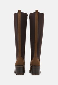 Botas marrones hasta la rodilla con un tejido liso, acentos de ante marrón en contraste, tacón cuadrado y cremalleras a los lados.