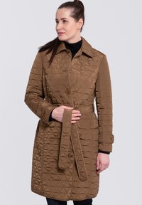 Abrigo acolchado marrón con collar, frente abotonado y cinturón. Presenta un patrón de diamantes y bolsillos, con mangas largas y un acabado texturizado.