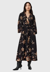 Vestido maxi negro con flores que presenta un escote en V profundo, mangas largas, cinturilla con lazo y una silueta fluida. Acentuado con patrones florales en beige y marrón.