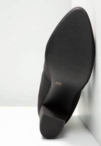 Zapato de tacón negro con superficie lisa, que cuenta con una suela de goma y una punta redondeada. Tamaño marcado como 37 en la suela.