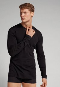 Schwarzes langärmliges Shirt aus weichem Stoff, mit V-Ausschnitt und taillierter Passform, kombiniert mit passenden schwarzen Shorts. Glatte Textur und minimalistischer Stil.