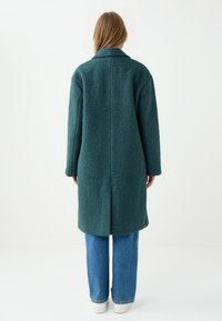 Lang, textuur rijk groen jasje met een notch-kraag, ellebooglange mouwen en een rechte snit, gecombineerd met brede denim en witte sneakers.