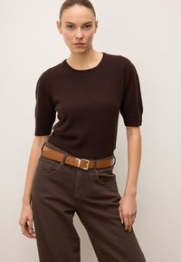 Barna, rövid ujjú kötött pulóver sötétbarna, magas derekú nadrággal és világosbarna övvel, amelynek téglalap alakú arany csatja van.