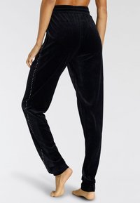 Schwarze Samthose mit lockerem Schnitt, ausgestattet mit einem Kordelzugbund und einer Reihe kleiner metallischer Nieten von der Hüfte bis zum Saum.