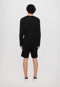 Camisa negra de manga larga y pantalones cortos negros. La tela es suave y tiene un corte relajado. Detalle del logo notable en la parte trasera de la camisa.