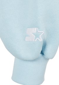 Light blue sweatshirt sleeve with ribbed cuff, featuring a white embroidered logo design of a star and stylized letter "S."