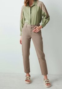 Grønstribet skjorte med beige blondeaccenter, lysebrune tætsiddende bukser og multicolore sandaler med blomsterdetaljer, placeret på en lys baggrund.