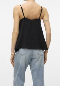 Top nero senza maniche con una vestibilità comoda, tessuto testurizzato e spalline regolabili, abbinato a jeans in denim blu chiaro.
