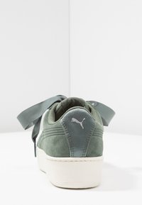 Grüne Wildledersneaker mit einer weißen Gummisohle, satinierten Schnürsenkeln und einem silbernen Puma-Logo an der Ferse. Glatte Textur und runde Zehenform.