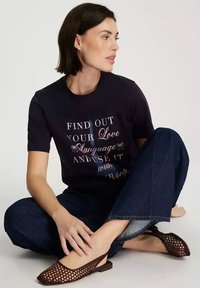 Granatowy t-shirt z nadrukowanym napisem w różnych czcionkach, w połączeniu z ciemnoniebieskimi, szerokimi spodniami dżinsowymi i brązowymi sandałami na obcasie z odkrytym palcem oraz wycięciem.