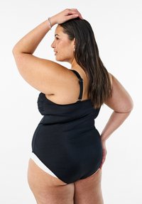 Costume da bagno nero con spalline regolabili, dettagli arricciati sul busto e un pannello bianco in contrasto sulla parte inferiore. Tessuto morbido.