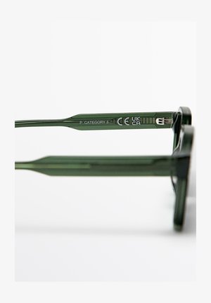 Close-up van een groen brillenpootje met daarop "P CATEGORY 3" en CE, UKCA-certificeringsmerken tegen een witte achtergrond.