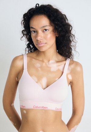 Roze draadloze beha met een diepe V-hals, zacht materiaal en een opvallend Calvin Klein-logo in contrasterend rood op de band.