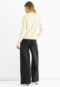 Cream ribbed sweater with long sleeves paired with high-waisted black wide-leg jeans and light-colored heeled shoes; back view.