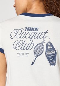Λευκό μπλουζάκι με ναυτικό μπλε γιακά. Το γραφικό σχέδιο περιλαμβάνει "NIKE Racquet Club," ρακέτα τένις και μπρελόκ. Το κείμενο π αρακάτω γράφει: "ΧΤΥΠΗΣΕ ΤΗ ΜΠΑΛΑ ΟΣΟ ΠΙΟ ΔΥΝΑΤΑ ΜΠΟΡΕΙΣ."