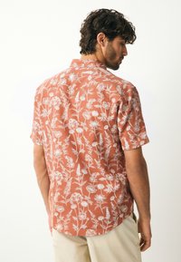 Chemise à manches courtes couleur corail avec motif floral blanc. Dotée d'un col pointu et d'une coupe décontractée, fabriquée en tissu léger.
