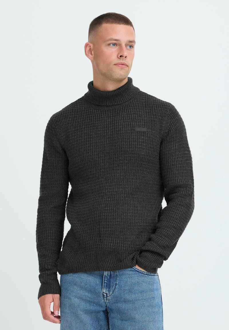 Maglione a collo alto di colore grigio scuro, con una struttura a nido d'ape, dallo stile aderente con maniche lunghe e polsini a costine. Dettaglio di branding minimale.
