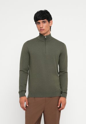 Olive green pullover sweater with high collar and quarter zip, ribbed cuffs and hem, soft texture, fitted design, worn with brown trousers.