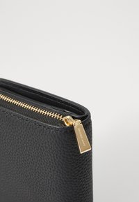 Black leather clutch with textured finish, gold zipper, and branded hardware detail. Compact rectangular shape with a top zipper closure.