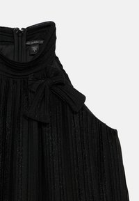 Czarna plisowana sukienka z zapięciem na zamek i dużą kokardą na ramieniu. Wykonana z błyszczącej tkaniny o teksturowanym wzorze.