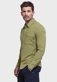 Grünes Langarmhemd mit Knopfleiste, zwei Brusttaschen und Logo am rechten Ärmel. Hergestellt aus einem glatten, leichten Stoff.