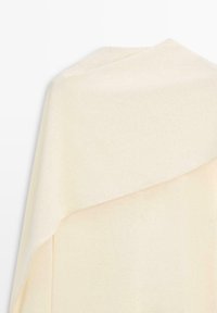 Écharpe en laine douce couleur crème, pliée avec une extrémité drapée sur l'autre sur un fond blanc.