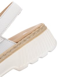 Primer plano de una sandalia de cuero blanca con plantilla beige acolchada y suela gruesa de goma blanca con relieve.