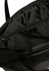 Interno di una borsa a tracolla sintetica nera con una texture liscia, dotata di una tasca con zip e un'etichetta con il logo. La fodera è anch'essa nera con un motivo sottile.