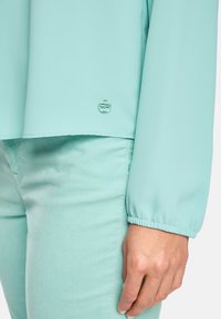 Lichtblauwe top met lange mouwen en elastische manchetten, gecombineerd met bijpassende lichtblauwe broek. Bevat een klein logo-detail op de top.