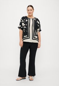 Top a maniche corte nero e crema con motivo a fantasia, caratterizzato da disegni astratti, abbinato a pantaloni neri a campana e sandali bianchi.