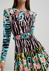 Robe multicolore à manches longues, présentant un motif rayé tigre rose et noir, des accents floraux, et une ceinture assortie.