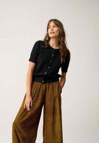 Svart kortärmad kofta med rund halsringning och knappstängning, kombinerad med högtalande, veckad byxor i rostfärg med ränder.