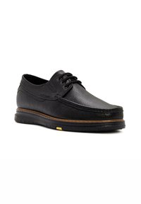 Chaussure en cuir noir à lacets avec une surface texturée, bout rond et coutures contrastées marron. Elle dispose d'une semelle en caoutchouc avec un accent jaune.