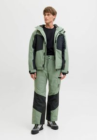 Outerwear set includes a light green jacket with black accents and matching trousers. Material appears waterproof with a sleek texture.