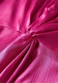 Tissu rose vif avec des plis réunis créant des plis texturés et un détail de nœud central sur un matériau lisse et brillant.