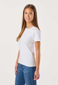 Hvid t-shirt med korte ærmer lavet af blød bomuld, med en enkel rund halsudskæring og en tætsiddende silhuet, kombineret med blå jeans.