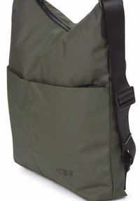 Bolso de hombro verde oliva hecho de tela suave, con cierre superior con cremallera, correa ajustable y bolsillo frontal. Logotipo de KCB impreso en un lado.