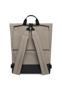 Béžový batoh s nastaviteľnými popruhmi, vrchným úchytom a čiernym dnom. Obsahuje klapkovú kapsu a pevné kovanie.