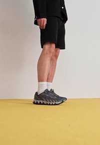 Hallid hallid spordijalatsid, millel on tekstureeritud pealmine osa, paks tallaosa punaste aktsentidega, koos valgete sokkidega ja mustade lühikestega.