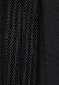 Tissu noir avec un panneau en maille comportant des découpes circulaires, adjacent à une surface en tissu lisse, les deux présentant de délicates finitions de couture.