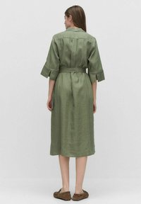 Olive green midi sukienka lniana z paskiem w talii, rękawami 3/4 i luźnym krojem. Posiada yoke z tyłu i kieszenie po bokach.