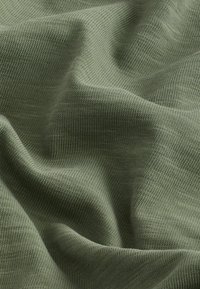 Groene gebreide stof met fijne textuur, met subtiele ribbels en een zachte, gladde oppervlakte, die in zachte plooien valt.