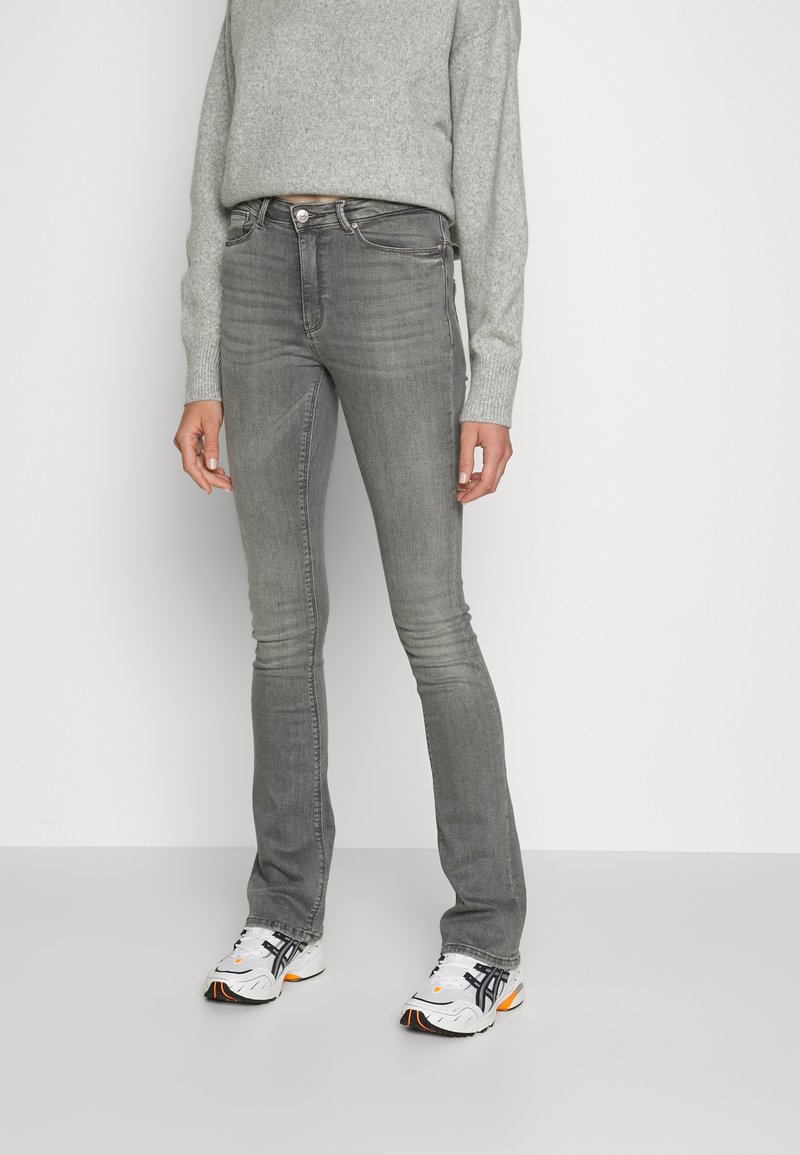 Jeans cinzas justos com uma ligeira boca de sino, apresentando uma cintura média e uma textura suavemente desbotada. Combinados com um suéter cinza claro e ténis desportivos.