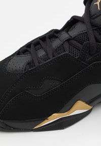Černá sportovní obuv s texturovaným svrškem, vybavená síťovinovými panely, zlatými akcenty a výrazným zakřiveným designem podrážky.