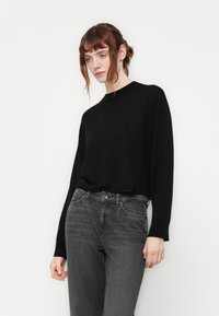 Maglione nero a maglia con collo rotondo e maniche lunghe, abbinato a jeans in denim grigi; texture liscia, vestibilità comoda, design minimalista.